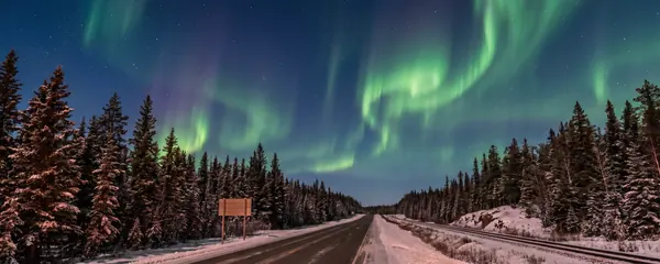 Northern highway and rail line under green aurora